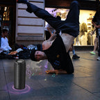 Person macht einen Handstand auf der Straße mit einem Meacode tragbaren Bluetooth-Lautsprecher und projizierten Musiknoten ringsum